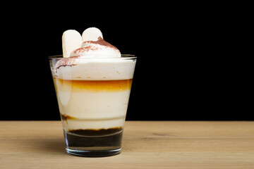 Tiramisu dessert in a glass on a wooden table in a restaurant with a black background