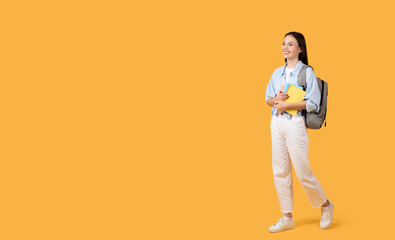 Fototapeta na wymiar Happy female student with backpack and notebooks on orange backdrop