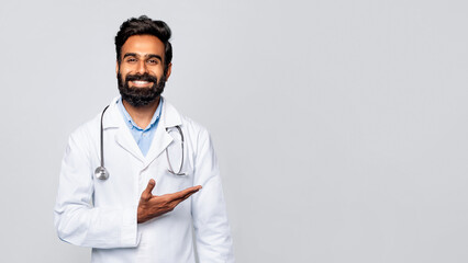 Inviting indian male doctor gesturing with hand aside on grey background