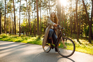 Young woman in stylish clothes rides a bicycle in a sunny park. Active lifestyle.