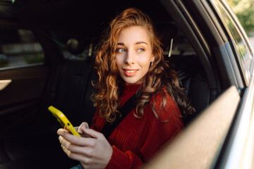 Beautiful young woman uses a smartphone while sitting in the back seat of a car. Woman talking on...