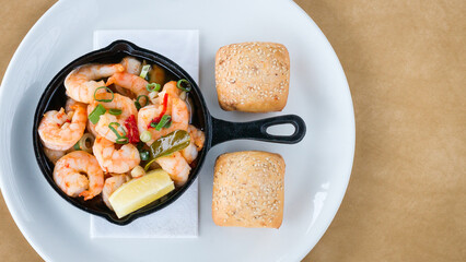 Top view of Garlic pan fried prawns on a white plate with sesame seed bread rolls