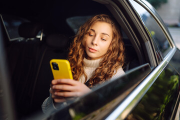 Beautiful young woman uses a smartphone while sitting in the back seat of a car. Woman talking on...