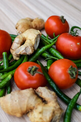 Fresh Ginger, Tomato and green chili pepper on plain wooden table, green essential vegetables for all essential foods, view of unpeeled vegetables with plain background