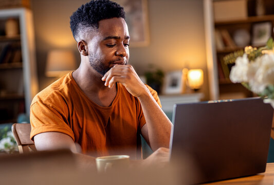 Young African American man sitting at home working while using laptop.