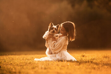Illuminated by sunlight. Cute little girl is on the field with dog