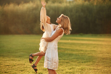 Holding girl in hands. Woman with her daughter is on the summer field