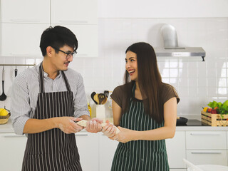 Asian man wearing eye glasses preparing bakery in modern kitchen with beautiful woman with long black hair. Asian young couple playing with  the dough that they made for pizza.