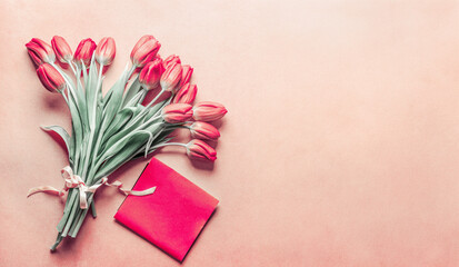Red tulips bunch with blank greeting card on pale background with copy space, top view