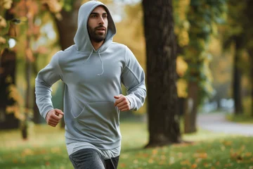 Deurstickers man jogging in park wearing a gray hooded sweatshirt © primopiano