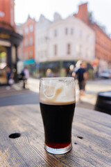 Close-up of pint of Guinness beer on a round table outside with a street background on a beautiful autumn morning in Dublin city Ireland - obrazy, fototapety, plakaty