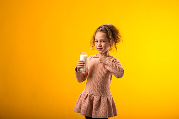 Smiling child girl holding glass of milk and pointing finger at it. Nutrition and health concept
