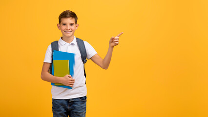 Happy schoolboy carrying backpack and textbooks and pointing aside at copy space
