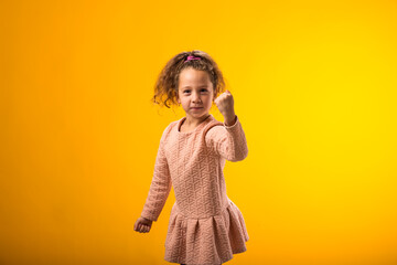 Enraged Child girl showing fist at camera on yellow background. Negative emotions concept