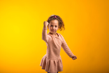 Enraged Child girl showing fist at camera on yellow background. Negative emotions concept