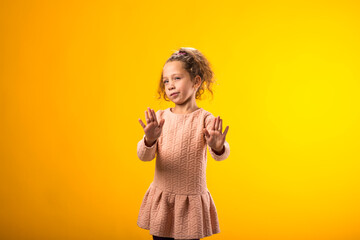 Child girl showing stop gesture on yellow background. Bulling and negative emotions concept