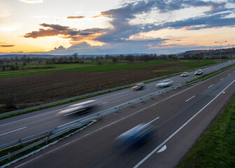 Cars drive at high speed on the highway through the rural landscape. Fast blurred highway driving....