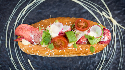 Close up of a lobster roll with tomato and avocado on a black plate