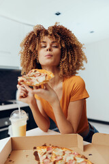 Woman enjoying a delicious slice of pizza in front of a plain cardboard box