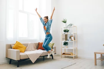 Foto op Canvas Joyful Woman Jumping and Dancing to Music in Home Apartment, Carefree and Happy © SHOTPRIME STUDIO