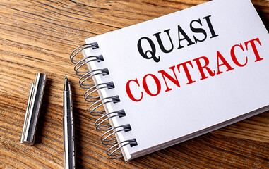 QUASI CONTRACT text on notebook with pen on wooden background