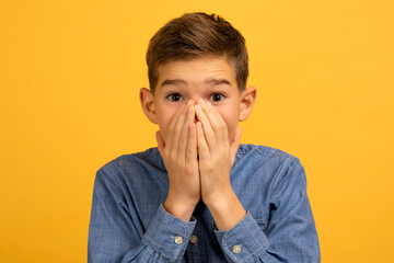 Teenage boy with shocked expression covering his mouth with both hands