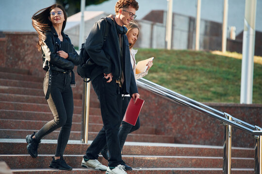 Walking down the stairs. Three young students are outside the university outdoors