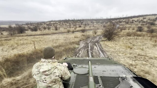 Infantry fighting vehicle with Ukrainian warrior in hatch moving along a dirt road on front line.