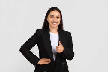 Smiling young businesswoman giving thumbs up, wearing black suit