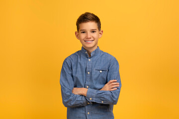 Confident teen boy in blue denim shirt standing with arms crossed