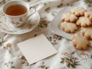 Obraz na płótnie Canvas Tea Time Scene, Porcelain Cup, Shortbread Cookies, and Blank Note Mockup on Floral Bed Linen