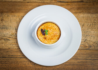 Top view of traditional French onion soup topped with cheese in white bowl on wooden table in restaurant