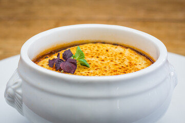 Close up of traditional French onion soup topped with cheese in white bowl on wooden table in restaurant