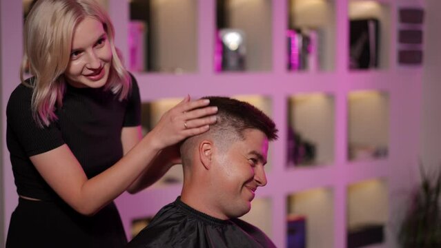 A beautiful girl hairdresser shows her work to a smiling male client and tells to him, how to take care of his hair in the future. Slow motion
