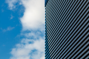 A minimalistic photo of a part of a modern building with repetitive pattern on its exterior stands out against the partly cloudy sky