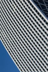 A minimalistic photo of a part of a modern building with repetitive pattern on its exterior stands out against the clear blue sky