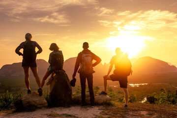 Four young hikers with backpacks and friends are enjoying great view at sea, islands and sunrise....