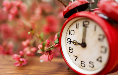 Flowers and red alarm clock. Spring forward, springtime or daylight savings time background. - 735959423