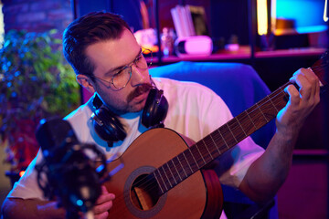 Guitarist recording music in vibrant studio with laptops and professional microphone in neon light...