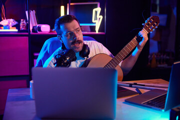 Artist composing music, vocalist playing on acoustic guitar in front of computer in neon light...