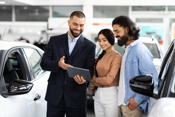 Auto dealer with digital tablet explains car features to couple