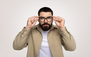 Serious smart millennial middle eastern man adjusting glasses, focused gaze, with thoughtful expression