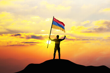 Armenia flag being waved by a man celebrating success at the top of a mountain against sunset or...