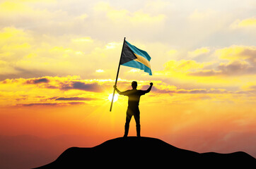 Bahamas flag being waved by a man celebrating success at the top of a mountain against sunset or...