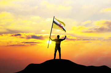 Brunei flag being waved by a man celebrating success at the top of a mountain against sunset or sunrise. Brunei flag for Independence Day. - obrazy, fototapety, plakaty
