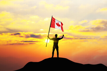 Canada flag being waved by a man celebrating success at the top of a mountain against sunset or...