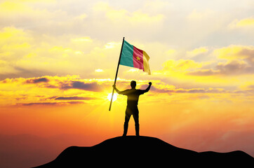 Cameroon flag being waved by a man celebrating success at the top of a mountain against sunset or sunrise. Cameroon flag for Independence Day.