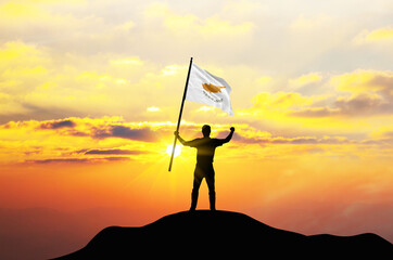 Cyprus flag being waved by a man celebrating success at the top of a mountain against sunset or sunrise. Cyprus flag for Independence Day.