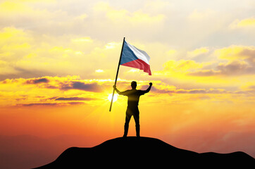 Czech Republic flag being waved by a man celebrating success at the top of a mountain against sunset or sunrise. Czech Republic flag for Independence Day.