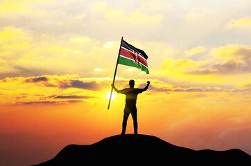 Kenya flag being waved by a man celebrating success at the top of a mountain against sunset or sunrise. Kenya flag for Independence Day.